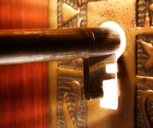 old fashioned key being inserted into a keyhole with white light shining behind it.