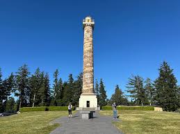 Astoria column against a blue sky and green pine trees